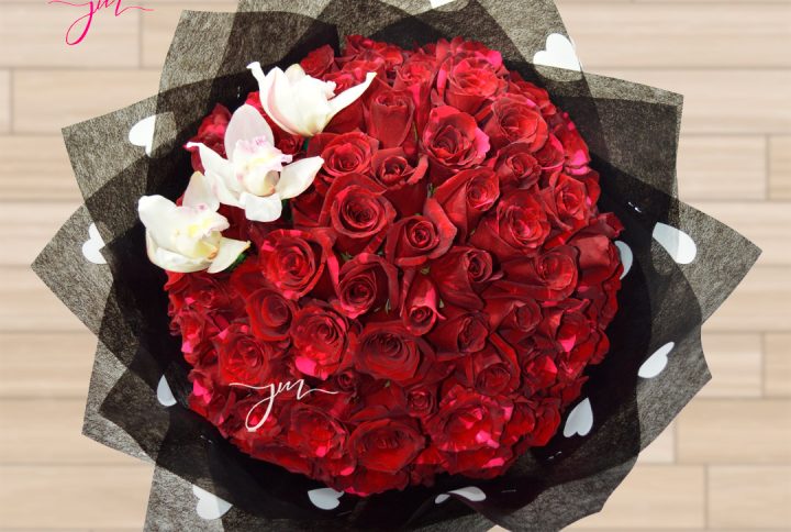 Bouquet de rosas rojas en empaque decorativo con orquídeas blancas sobre un fondo elegante.