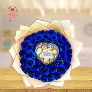 Ramo de rosas azules intensas con chocolates Ferrero Rocher en el centro, envuelto en papel crema y blanco.