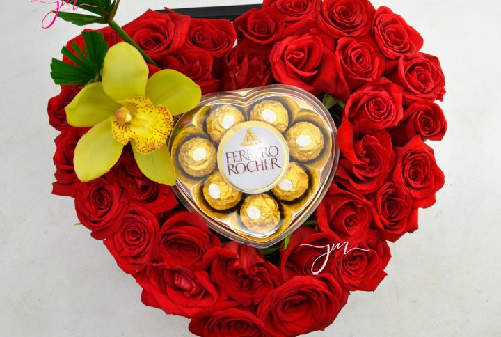 Arreglo floral en forma de corazón con rosas rojas, chocolates Ferrero Rocher y una orquídea amarilla.