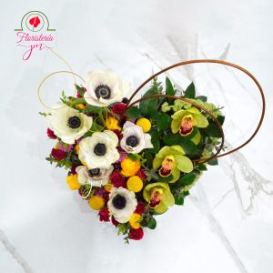 Arreglo floral en forma de corazón con anémonas blancas, orquídeas verdes y flores multicolores, decorado con detalles elegantes.