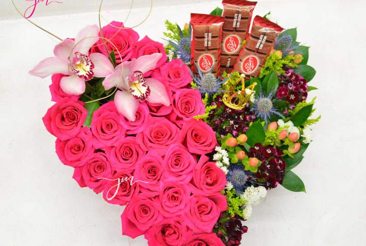 Arreglo floral en forma de corazón con rosas rosadas, orquídeas, flores multicolores y chocolates decorativos.