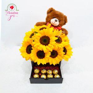 Arreglo floral con girasoles vibrantes, chocolates Ferrero y un oso de peluche.